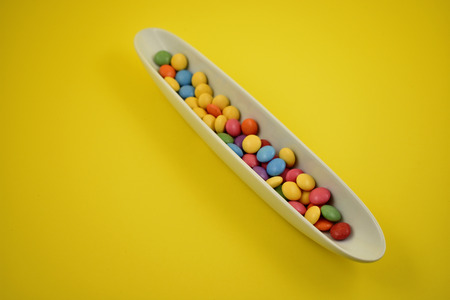 Colorful lentils stock images. Colorful candies on a yellow background. Chocolate lentils snack. Colorful candy in a white bowlの写真素材