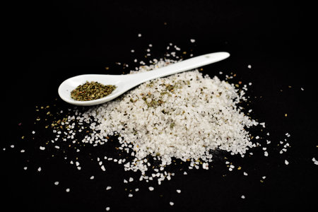 Herbal salt stock images. White salt on a black background. Pile of salt with a spoon images. Grained herbal saltの写真素材