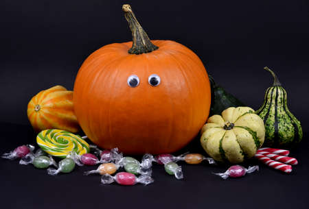 Spooky halloween pumpkin with eyes and candies stock images. Different types of pumpkins and squash autumn still life stock images. Decorative halloween pumpkins on a black background stock photoの写真素材