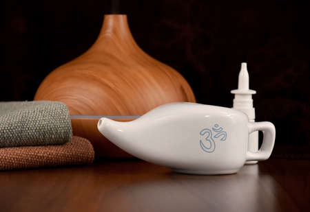 Ceramic Neti pot for nasal cleansing stock images. Nasal care images. White ceramic Neti pot with OM symbol stock photo. Neti pot still life with wooden humidifier and nasal spray imagesの写真素材