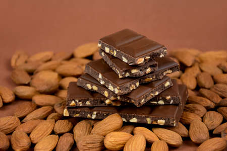 Milk chocolate cubes on heap with almonds stock images. Pieces of almond chocolate on a brown...