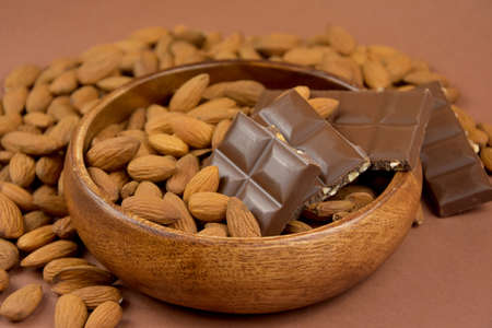Milk chocolate bar with almonds in a wooden bowl stock images. Almond chocolate in a bowl on a brown background close-up stock imagesの写真素材
