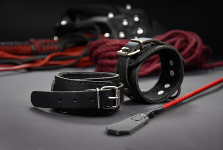 Leather handcuffs and a whip stock photo images. Sex toys for BDSM images. Set of erotic toys for adults only on a dark backgroundの写真素材