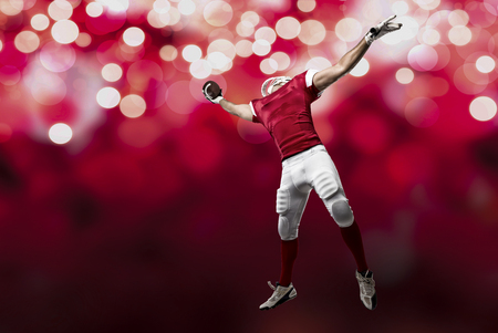 Football Player with a red uniform making a catch on a red lights background.の写真素材