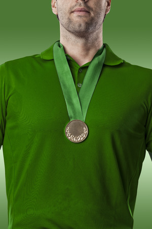 Golf Player in a green shirt celebrating with a golden medal, on a green Background.の写真素材