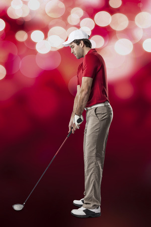 Golf Player in a red shirt taking a swing, on a red lights Background.の写真素材