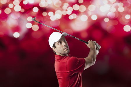 Golf Player in a red shirt taking a swing, on a red lights Background.の写真素材