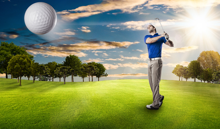 Golf Player in a blue shirt taking a swing, on a golf course.の写真素材