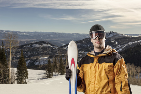 Skier with a yellow jacket, holding a pair of skis on a snowy mountain.の写真素材