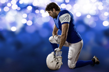 Football Player with a blue uniform on his knees, on a blue lights background.の写真素材