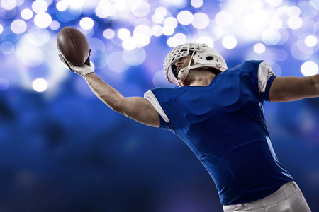 Football Player with a blue uniform making a catch on a blue lights background.
