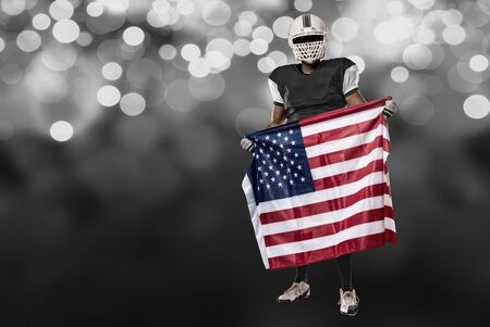 Football Player with a black uniform and a american flag, on a black lights background.の写真素材