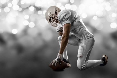 Football Player with a white uniform on his knees, on a white lights background.の写真素材