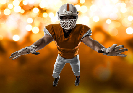 Football Player with a orange uniform making a tackle on a orange lights background.