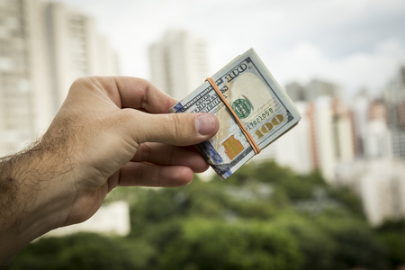 Hand of man holding dollar bills in front of a city landscape