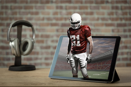 Football Player with a red uniform Playing playing and coming out of a tablet. Watching a football game on demand concept.の写真素材