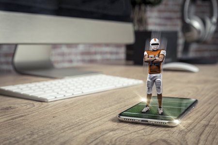 Football Player with a orange uniform playing and coming out of a full screen phone on a wooden...