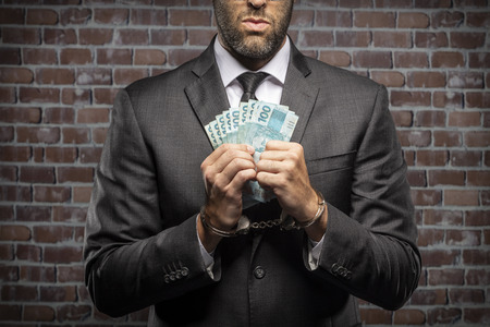 Brazilian man holding bills of money with a handcuff in a jail. concept of corruption, corrupt...