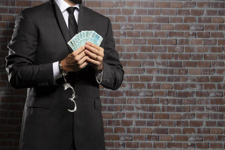 Brazilian man holding bills of money with a handcuff in a jail. concept of corruption, corrupt politicians, illegal businesses. brick background.の写真素材