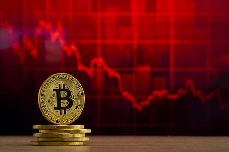 physical bitcoin standing at a wood table in front of a red graph. Bitcoin Bear Market conceptの写真素材