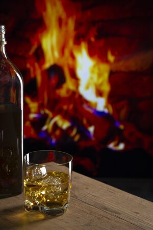 Glass of whiskey with ice on a wooden table in front of a fireplaceの写真素材
