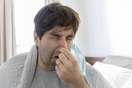a sick man, with a blanket over his back, sneezing and coughing.の写真素材