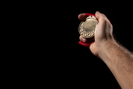 hand holding a gold medal on black with blank face for text, concept for winning or success