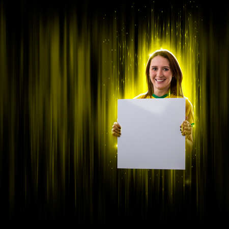 Brazilian woman fan, holding white empty board on a black and yellow background with copy space.の写真素材