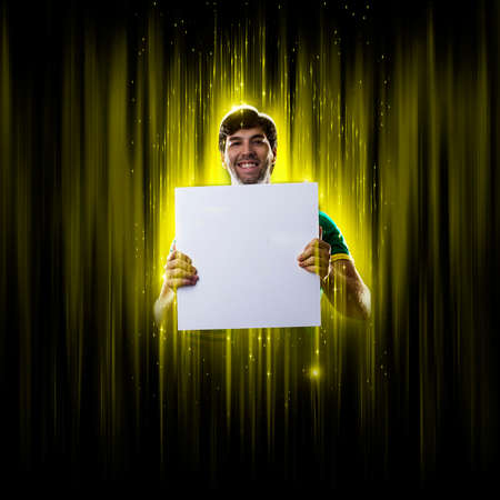 Brazilian fan, holding white empty board on a black and yellow background with copy space.の写真素材