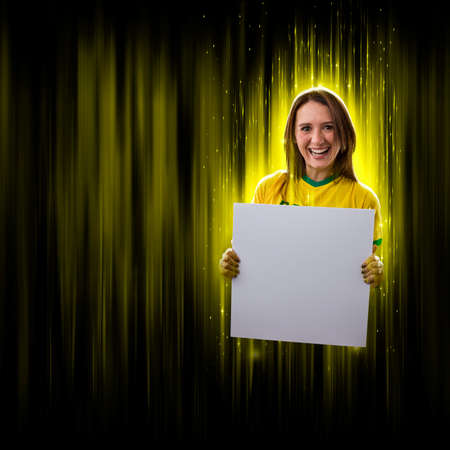 Brazilian woman fan, holding white empty board on a black and yellow background with copy space.の写真素材
