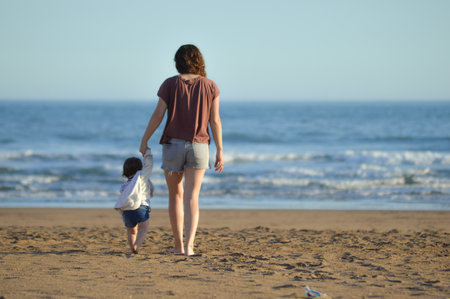 Mother and son walking on the beach at the day time. People having fun outdoors. Concept of friendly...