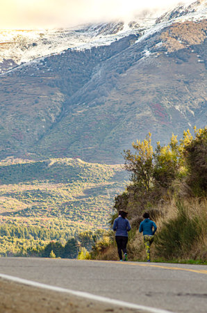 Rear view of a friends running on a mountain road in autumnの写真素材