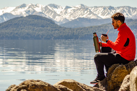 Young man sitting on a rock by the lake drinking Argentine mateの写真素材
