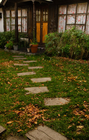 Old wooden house in the autumn garden with grass, leaves and flowersの写真素材