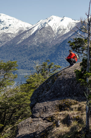 Hiker sitting on top of a rock and looking at the lakeの写真素材