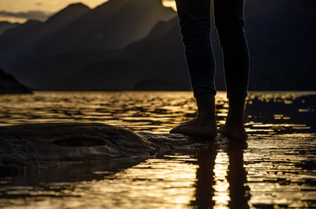 Feet of a woman standing on the rock in the water at sunsetの写真素材