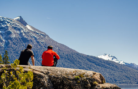 Young couple sitting on a rock looking at the lake and mountains in the backgroundの写真素材