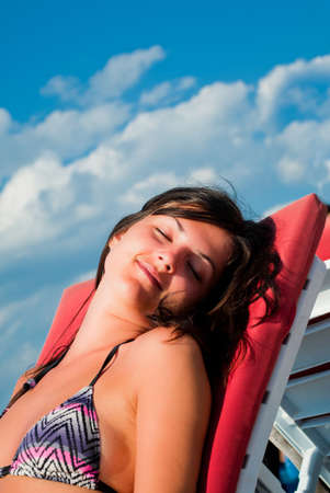 Beautiful girl enjoying the sun at the seaside on a beach chairの写真素材