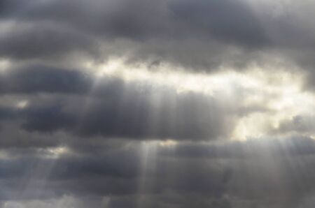 Rain clouds color: gray, dark blue. White light shines from behind the clouds. The sun's rays...