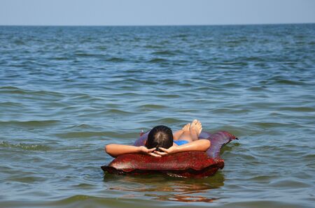 A teenager lies on an air mattress in the sea and enjoys the peace. The boy is relaxed and dreamy...