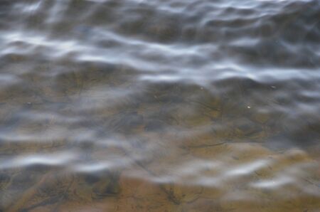Sunny beach. The bottom of the river is visible through the waves of water.