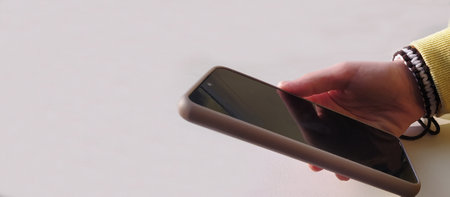 The teenager is holding a mobile phone in his hand. At close range. A girl's hand with a phone on a light background. Handmade bracelet, decoration. Online communication, modern technologies.の写真素材
