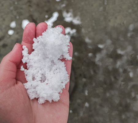 Small hail in the man's hand. Top view. Granulated snow in the person's hand. At close range. The...