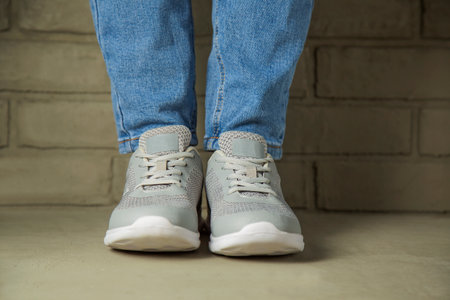 A woman in white sneakers stands against a brick wall in the background. Feet in sports shoes without a brandの写真素材