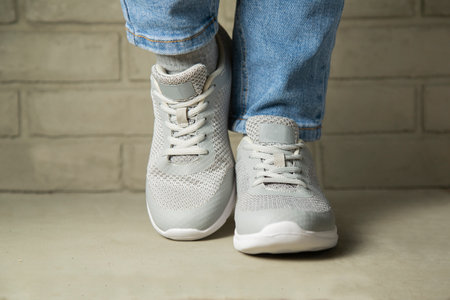 Modern young woman in stylish jeans in fashionable youth sneakers stands near wall in the city....