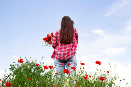 Nature and the field a girl with flowers in her hands on the background of wild flowers and the sky. A girl with long hair is standing with her back.の写真素材