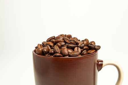 Coffee beans lie in brown mugs. On a white background. Roasted coffee seeds. Close-up.の写真素材