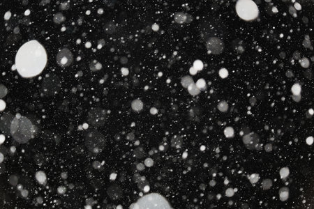 The bokeh is white on a black background. Snowfall winter. Light and light snowflakes on a dark background.の写真素材