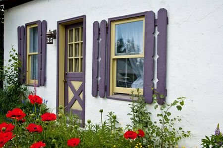 Little white house with purple shutters and flowersの写真素材