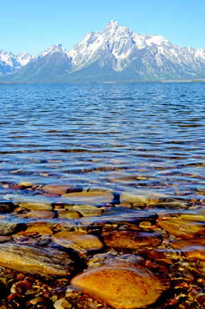 Beautiful lake water and stones beneath snow capped mountains.の写真素材